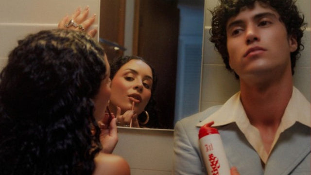 Man holding Riggs No.2 Curly Primer in a retro bathroom, woman reflected in the mirror